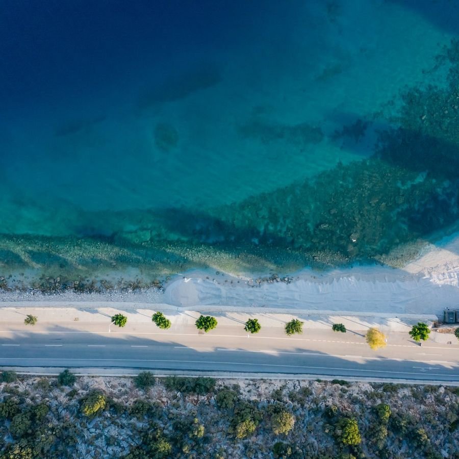 An aerial view of a coastal road running along a turquoise shoreline