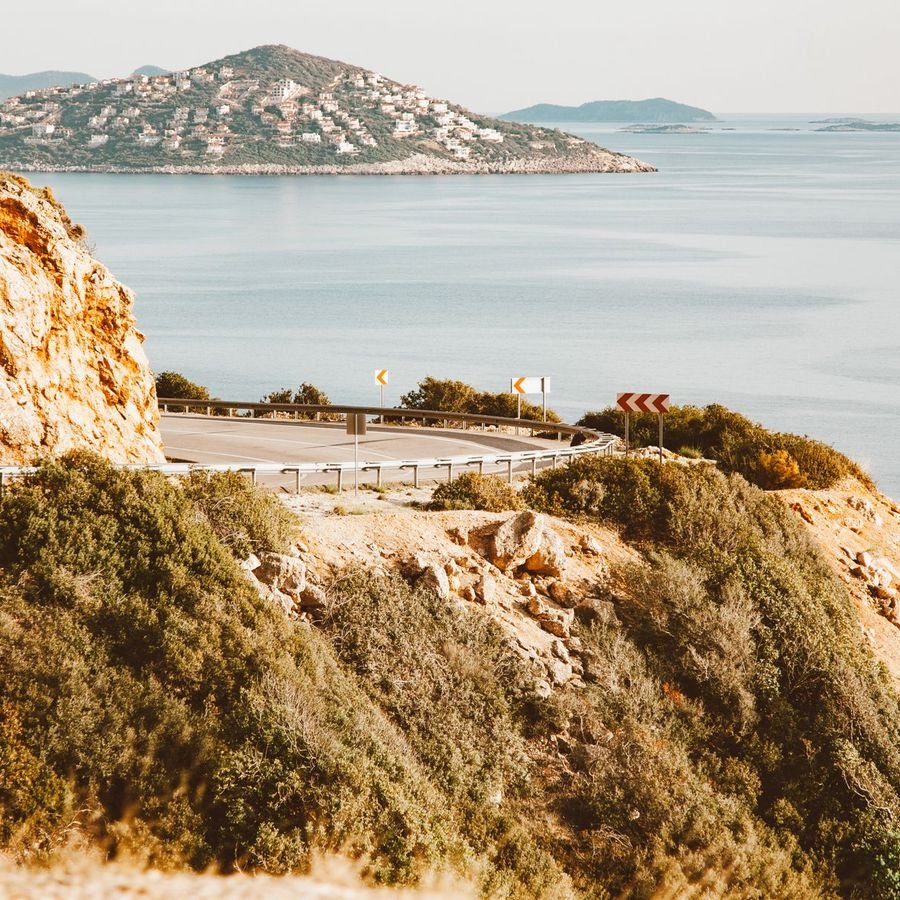 A coastal road curving around a limestone cliff above a calm blue sea