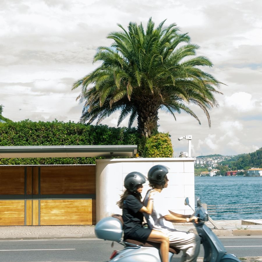 A couple riding a Vespa together along a sunny seaside road