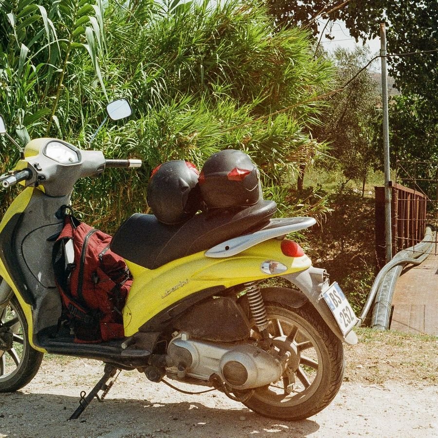 Two helmets resting on the seat of a scooter parked in bright Mediterranean sun