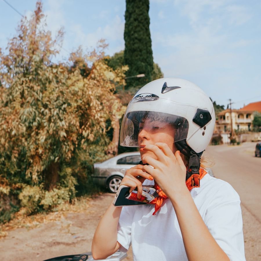A rider fastening the chin strap of a white open-face helmet on a sunny road