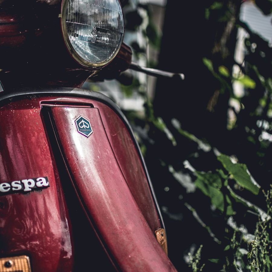 Close-up of a red Vespa's round chrome headlight and Piaggio badge