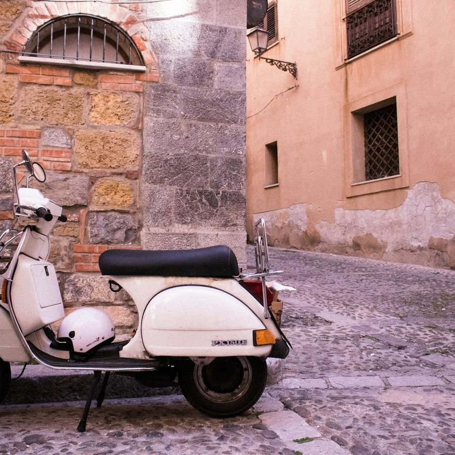 A classic white Vespa with a helmet on the handlebars in a stone old-town alley