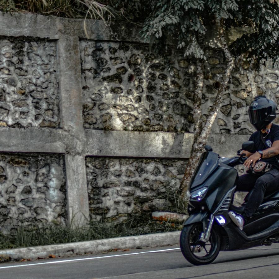 A rider on a Yamaha scooter on a coastal road beside a stone wall