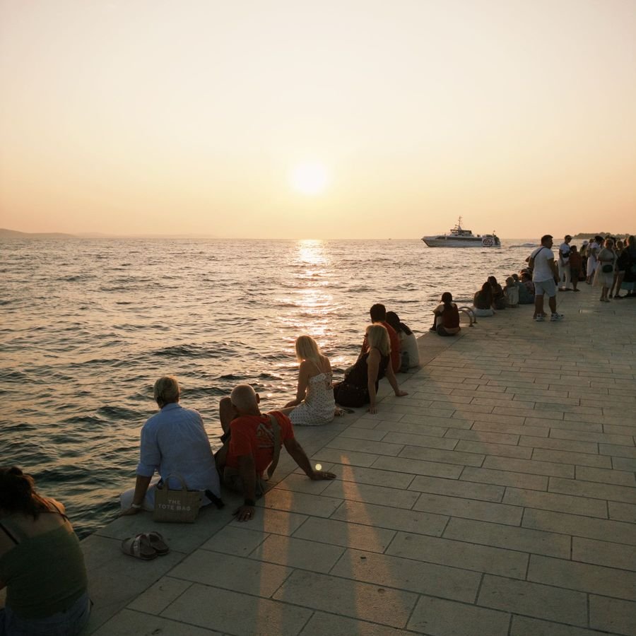 People sitting on the warm stone of the Zadar Riva watching the sunset